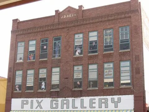 Exterior view of a multi-story brick building with painted window figures and a storefront sign.