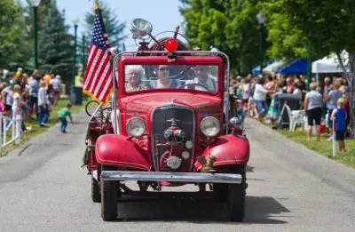 A vintage red fire truck drives down a street lined with spectators.