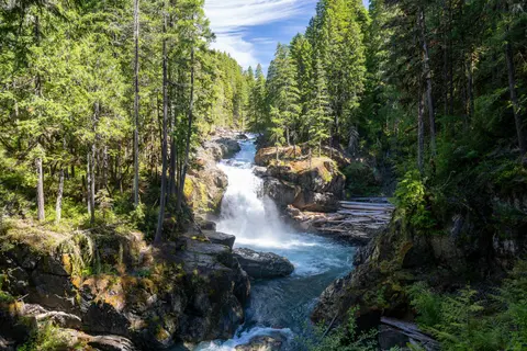 A waterfall flows through a rocky gorge surrounded by a dense green forest.