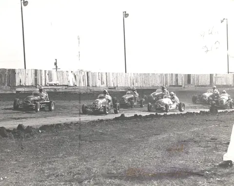 Historic black and white photograph showing vintage race cars on a dirt track.