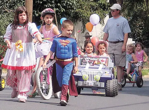 Children and an adult in costumes and riding vehicles during a parade on a street.