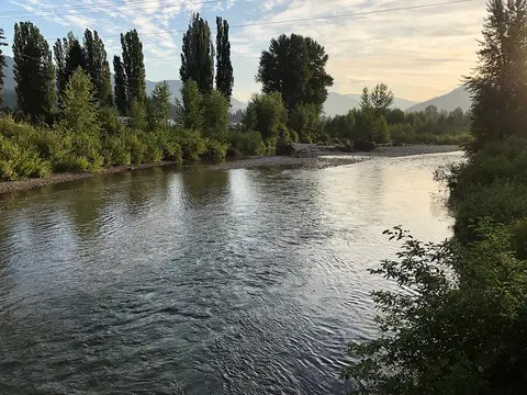 A river flows through a valley surrounded by trees and distant mountains.