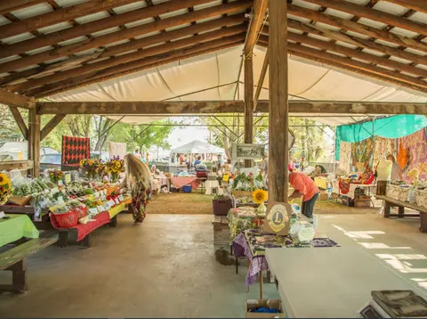 A craft and produce market is set up underneath a large open pavilion.