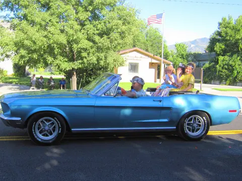 A blue convertible car drives down a street with children in the back.