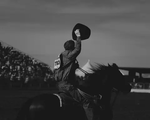 A cowboy on a horse waving his hat in an arena.
