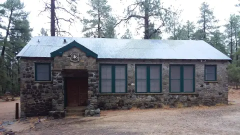 Exterior view of a stone building with a metal roof surrounded by trees.