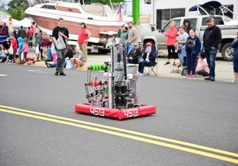 A robot operates on a street during an outdoor event with spectators.