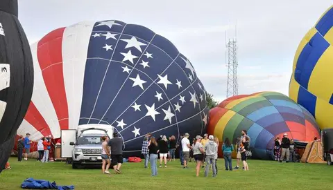 A group of people standing near large hot air balloons on a field.