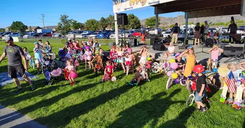 A group of children and adults gathered on a grassy area in front of a stage with bicycles.