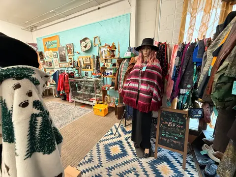 An interior view of a vintage shop showcasing clothing racks, a mannequin, and displays on a pegboard wall.