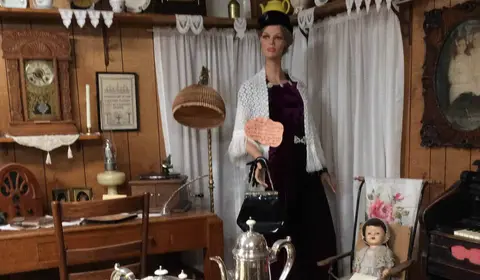 An interior view of a room display with a mannequin in period dress.