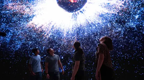 People looking up at a dome display showing a starry sky and galaxy.