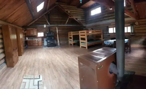 Inside view of a rustic log cabin with wooden furniture and a stove.