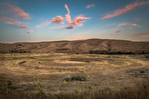 A landscape view of rolling hills and a colorful sunset sky over a field.