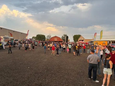 A large crowd of people gathers outdoors at an event with food trucks and a red barn.
