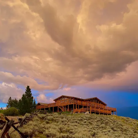 A large wooden lodge sits on a hill under a dramatic cloudy sky.