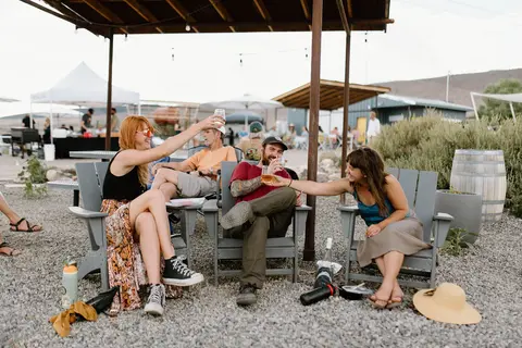 A group of friends sitting in outdoor chairs, having drinks and laughing under a shelter.