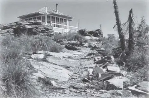 A historic black and white photograph showing a lookout building on a rocky hilltop.