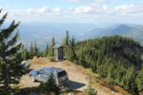 A vehicle parked on a mountain ridge with a small outhouse and scenic view.