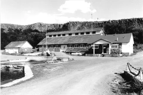 A historic black and white photograph shows stone buildings and a pool in a landscape.