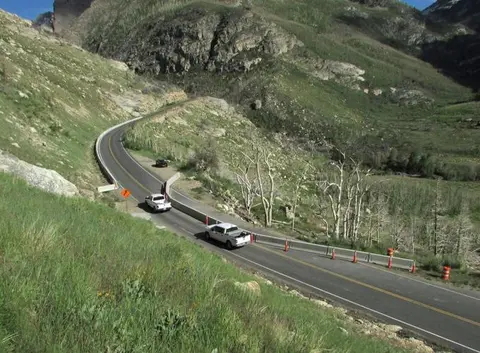 A high-angle view of a winding road cutting through a mountain landscape with several vehicles.