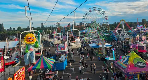 A view of a carnival from a ski lift with a ferris wheel in the background.