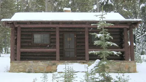 A log cabin covered in snow in a forest.