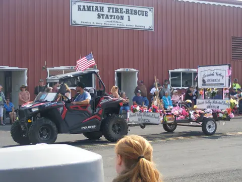 A parade float pulled by an all-terrain vehicle passes a fire station.