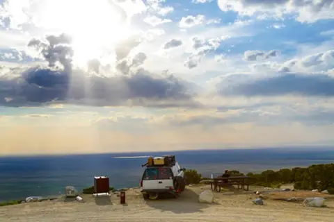 A car parked at an overlook with a view of a vast landscape under a cloudy sky.