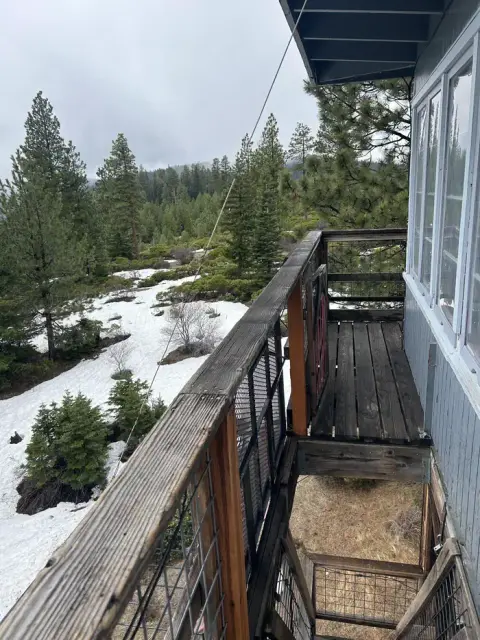 A view from the wooden balcony of a building overlooking a snowy, forested landscape.