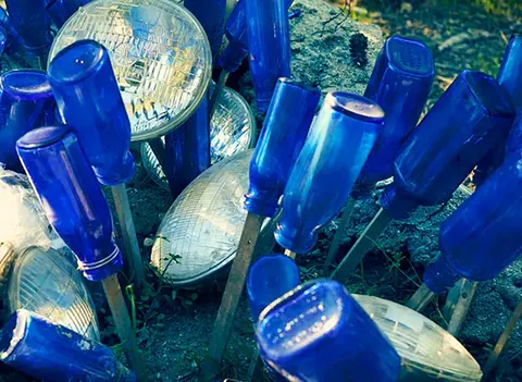 An arrangement of blue glass bottles and vehicle headlights outdoors.