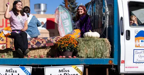 Two young women ride on a decorated truck float in a parade.