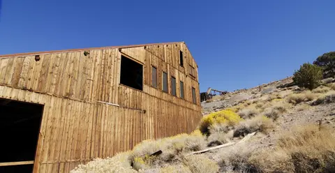 An old wooden building sits on a dry hillside under a clear blue sky.