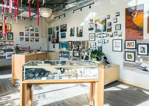 An interior view of a shop showcasing numerous framed paintings on the walls and display cases with jewelry.