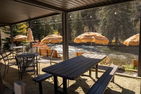 A covered outdoor seating area with picnic tables and chairs next to a rushing river.