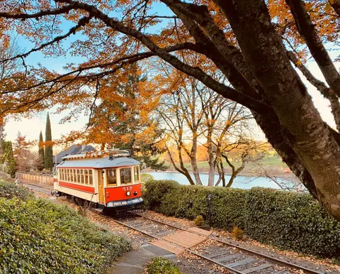 A vintage trolley travels along tracks near a river surrounded by autumn foliage.