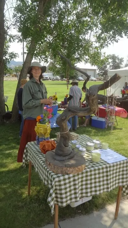 A woman stands behind a display table outdoors at a fair or market.