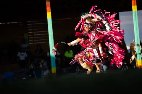 A person in colorful traditional regalia dances outdoors.