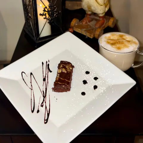 A chocolate dessert on a square plate next to a cup of coffee and a lantern.