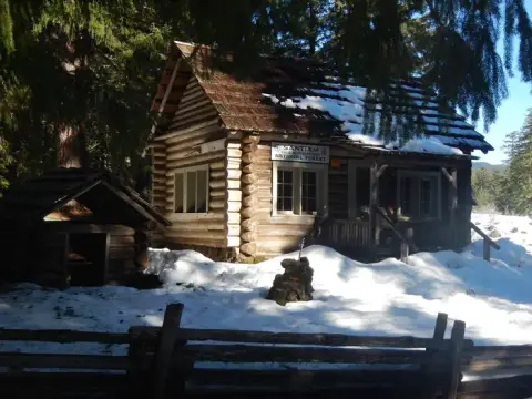 A log cabin surrounded by snow and trees with a sign on the front.