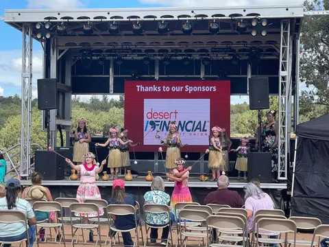 A hula dance performance takes place on an outdoor stage before a seated audience.