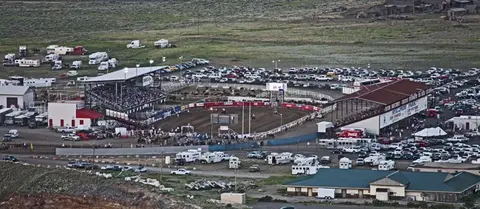 An aerial view of an outdoor rodeo arena surrounded by parked cars and trailers.