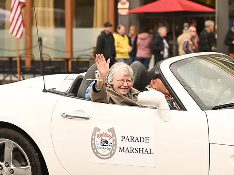 An older woman waving from a white convertible labeled parade marshal.