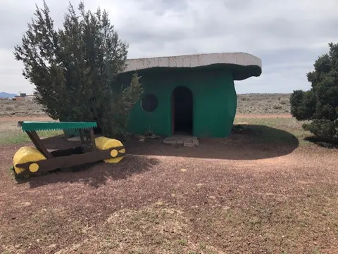 A whimsical green building resembling a prehistoric dwelling stands outdoors with a matching vehicle sculpture.