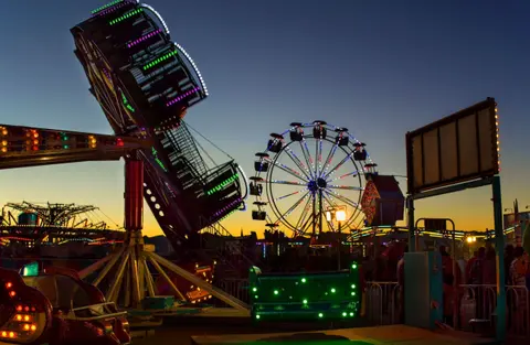 Lit amusement park rides operate at twilight.