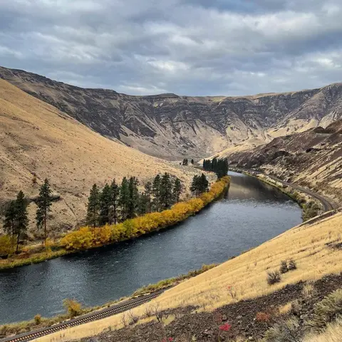 A wide river flowing through a dry canyon with a railway track along its bank.