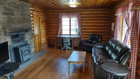 A rustic log cabin interior with a stone fireplace, wood walls, and leather furniture.
