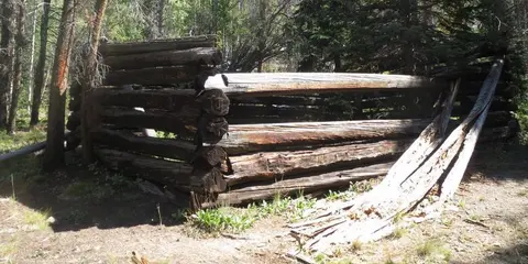 An old log cabin ruin stands in a wooded area.
