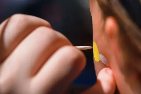 A close-up of a person having face paint applied to their cheek.