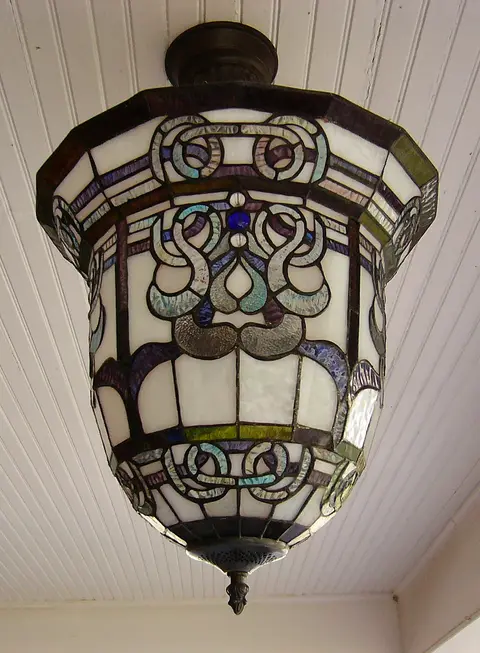 A close-up view of an ornate stained glass light fixture mounted on a white paneled ceiling.